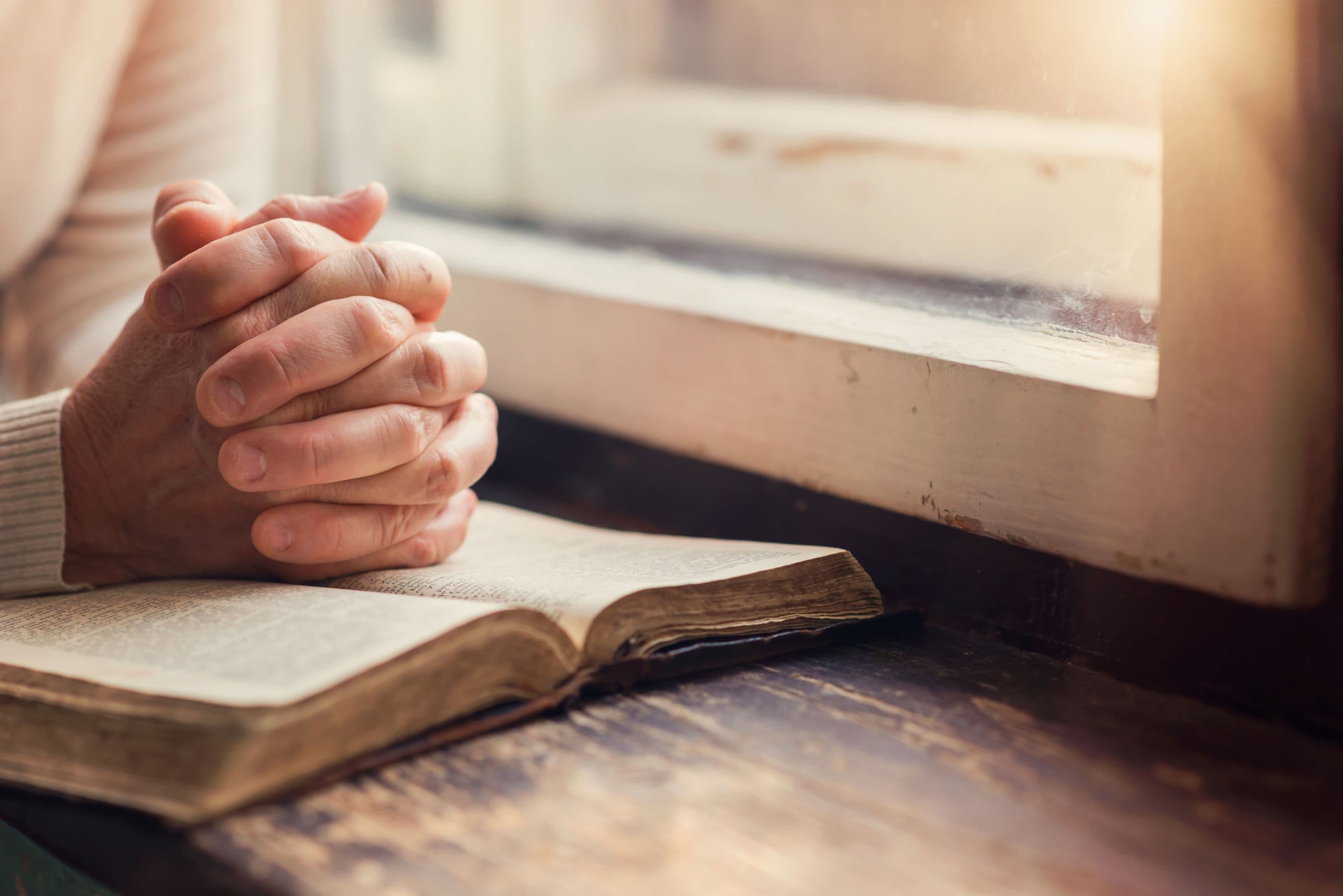 Hands clasped in prayer over an open Bible